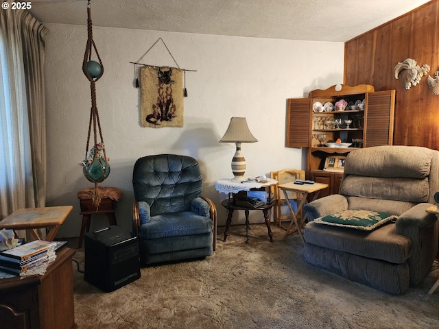 sitting room featuring carpet, wooden walls, and a textured ceiling