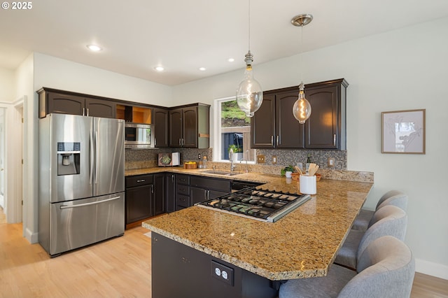 kitchen featuring stainless steel appliances, a sink, a peninsula, tasteful backsplash, and recessed lighting