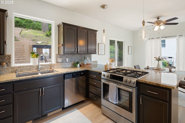 kitchen featuring appliances with stainless steel finishes, a sink, a peninsula, tasteful backsplash, and light wood-style flooring