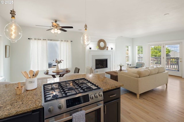 kitchen with stainless steel gas range oven, a glass covered fireplace, light wood-style floors, open floor plan, and hanging light fixtures