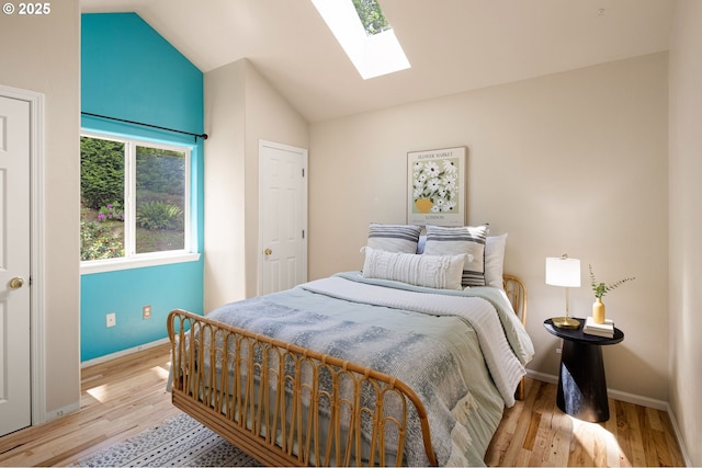 bedroom featuring a skylight, vaulted ceiling, light wood-style flooring, and baseboards