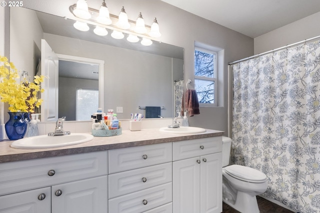 full bathroom featuring toilet, a healthy amount of sunlight, a sink, and double vanity