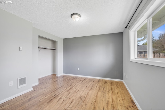 unfurnished bedroom featuring a textured ceiling, baseboards, visible vents, light wood-style floors, and a closet
