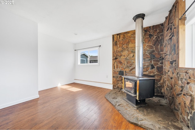 unfurnished living room with wood-type flooring, baseboards, and a wood stove