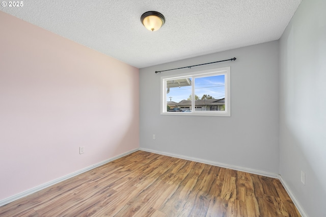 spare room with light wood-style floors, a textured ceiling, and baseboards