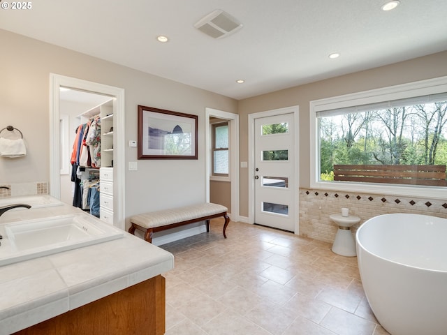 bathroom with double vanity, visible vents, a freestanding tub, a sink, and recessed lighting