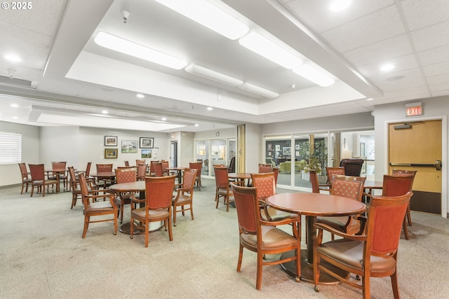 dining space with light carpet, a paneled ceiling, french doors, and a raised ceiling