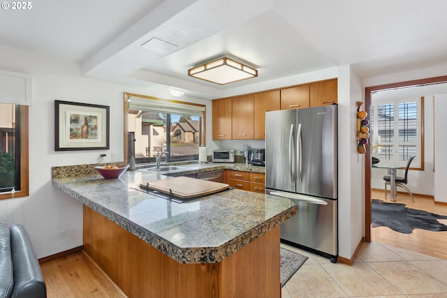 kitchen featuring stainless steel fridge, kitchen peninsula, sink, and a wealth of natural light