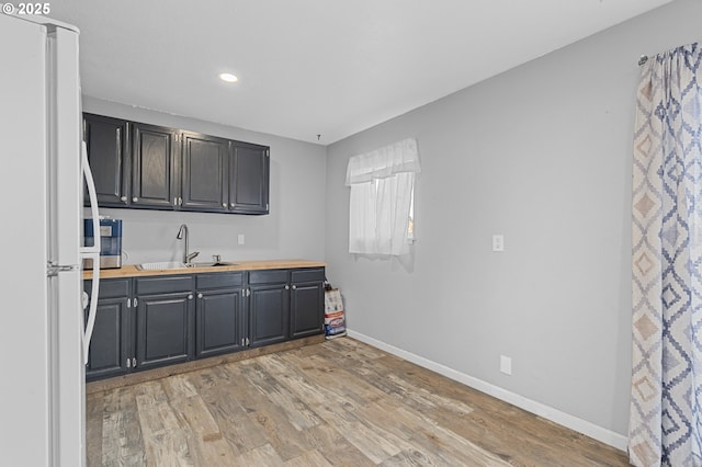 kitchen with white refrigerator, butcher block counters, light hardwood / wood-style floors, and sink