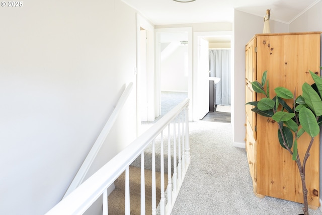 hall with ornamental molding, baseboards, light colored carpet, and an upstairs landing