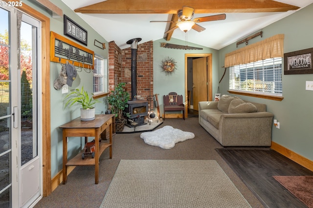 living area featuring vaulted ceiling with beams, ceiling fan, wood finished floors, baseboards, and a wood stove