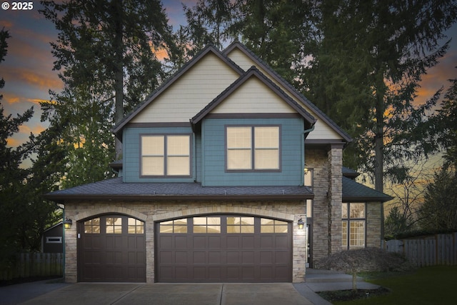 view of front of home with stone siding, a shingled roof, concrete driveway, and fence