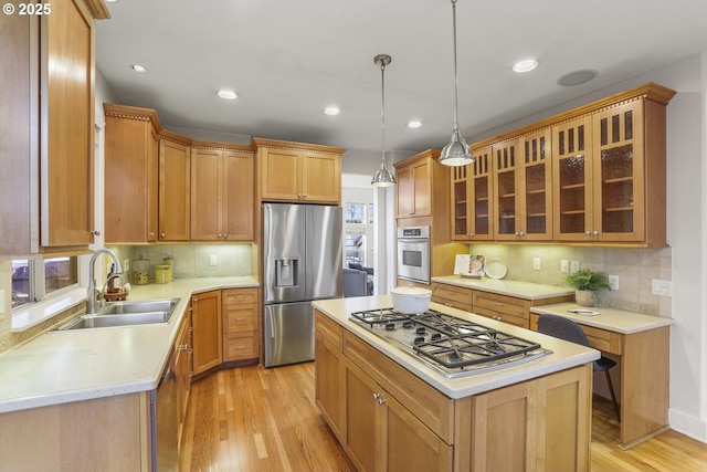 kitchen with stainless steel appliances, a sink, light countertops, light wood-type flooring, and a center island