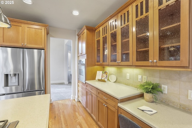 kitchen featuring light wood-style flooring, recessed lighting, stainless steel appliances, tasteful backsplash, and glass insert cabinets