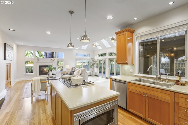 kitchen with stainless steel appliances, a sink, open floor plan, a center island, and a glass covered fireplace