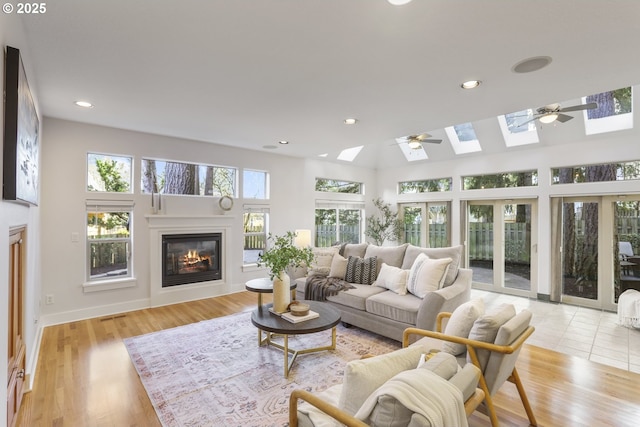 living room with light wood-type flooring, a glass covered fireplace, a ceiling fan, and a skylight