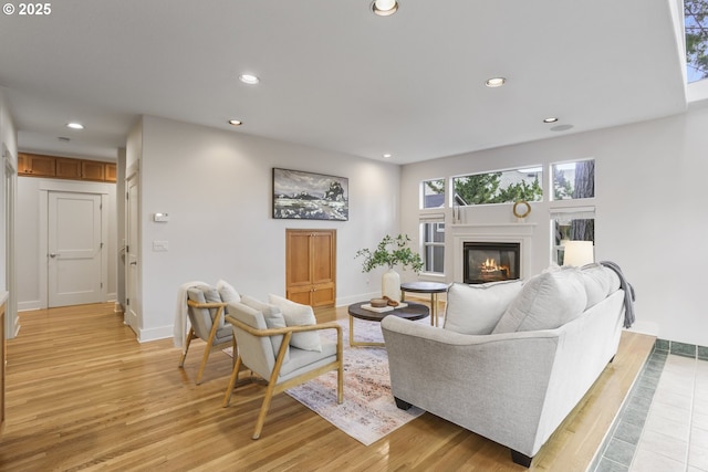 living room with baseboards, a glass covered fireplace, light wood-style flooring, and recessed lighting