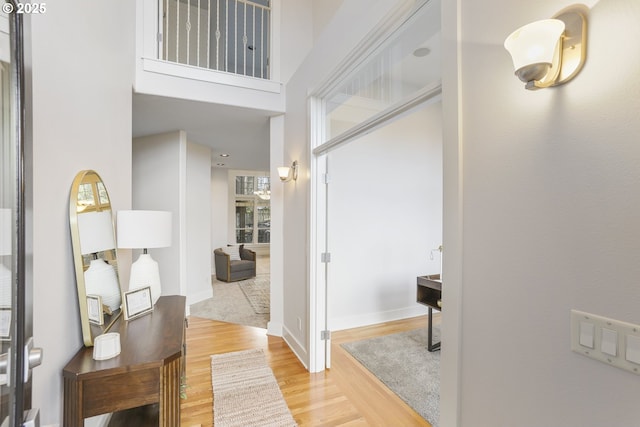 corridor with a towering ceiling, baseboards, and wood finished floors