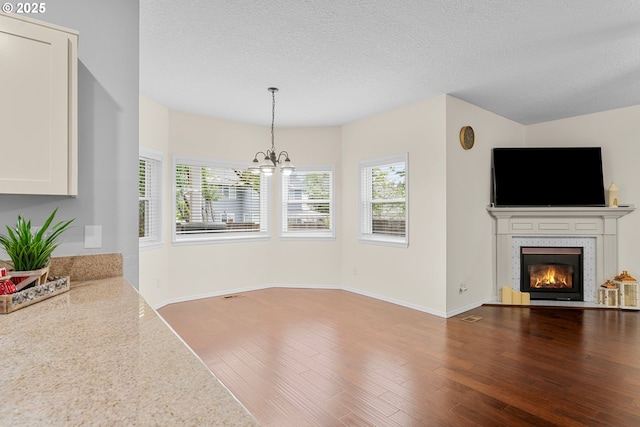 11769 SW 129th Pl, Tigard, OR 97223 - unfurnished living room featuring wood finished floors, a chandelier, a glass covered fireplace, healthy amount of natural light, and a textured ceiling