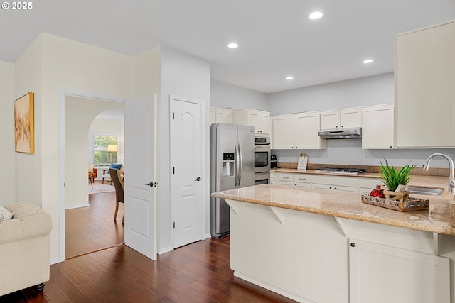 11769 SW 129th Pl, Tigard, OR 97223 - kitchen with stainless steel appliances, under cabinet range hood, a sink, arched walkways, and a peninsula