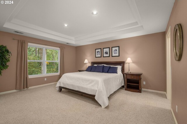 bedroom with a raised ceiling and light colored carpet