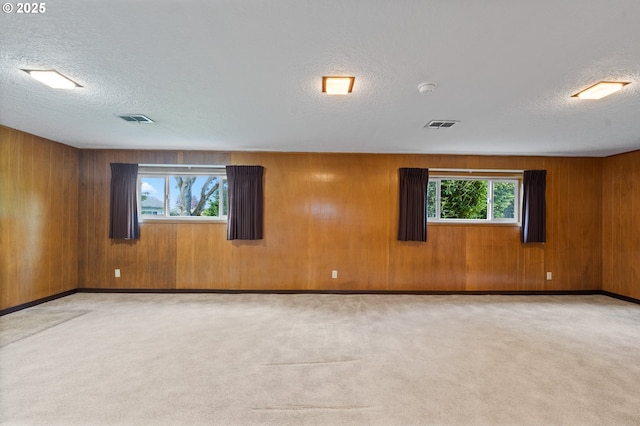 carpeted empty room featuring a textured ceiling, wood walls, and baseboards