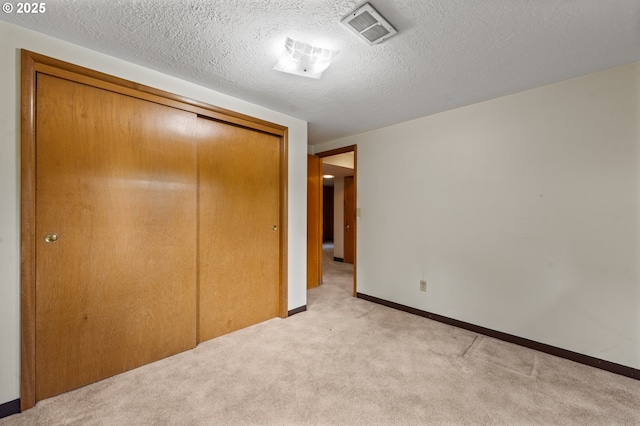 unfurnished bedroom with a closet, light carpet, baseboards, and a textured ceiling