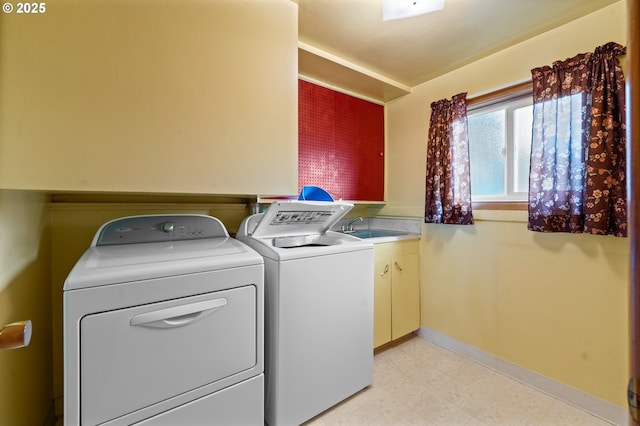 clothes washing area with washing machine and clothes dryer, cabinet space, and baseboards