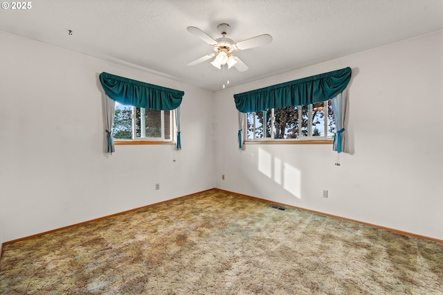 carpeted empty room with healthy amount of natural light, a ceiling fan, and baseboards