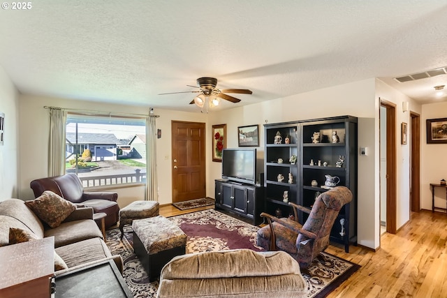 living room featuring ceiling fan, light hardwood / wood-style flooring, and a textured ceiling