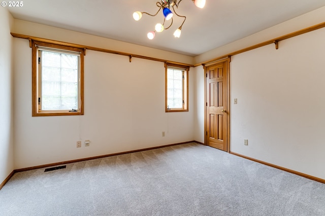 carpeted spare room with visible vents, baseboards, and an inviting chandelier