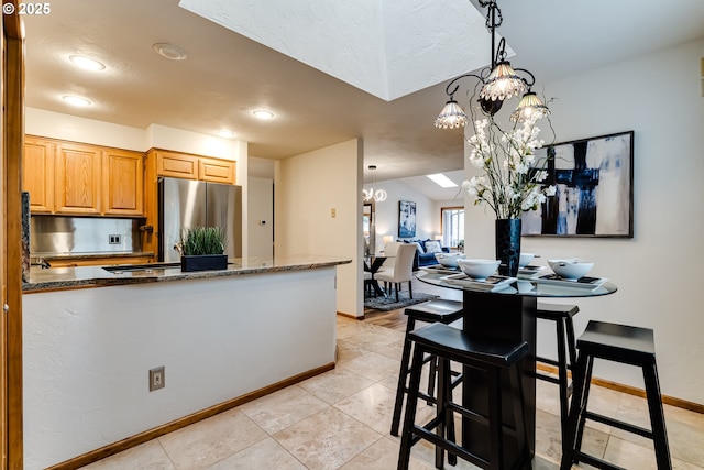 kitchen featuring hanging light fixtures, dark stone countertops, freestanding refrigerator, and baseboards