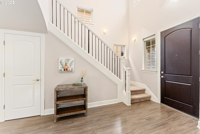 entryway featuring stairs, wood finished floors, baseboards, and a towering ceiling