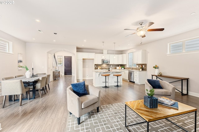 living area with baseboards, light wood-style flooring, recessed lighting, arched walkways, and ceiling fan