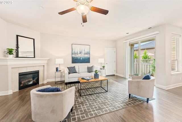 living room featuring visible vents, baseboards, wood finished floors, and a tiled fireplace