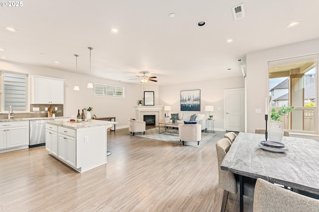 kitchen with visible vents, light wood-type flooring, a sink, a glass covered fireplace, and dishwasher