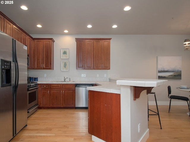 15320 SW Jasper Ln, Beaverton, OR 97007 - kitchen featuring appliances with stainless steel finishes, a peninsula, light wood-type flooring, a breakfast bar area, and recessed lighting