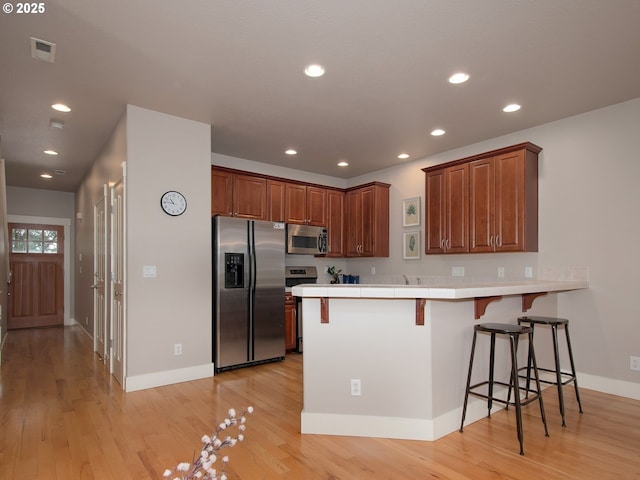 15320 SW Jasper Ln, Beaverton, OR 97007 - kitchen featuring appliances with stainless steel finishes, a peninsula, a kitchen bar, light wood-type flooring, and recessed lighting