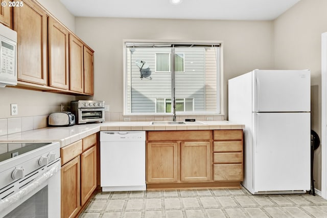 kitchen featuring a sink, white appliances, light floors, and tile countertops