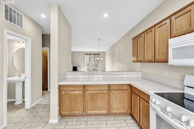 kitchen with visible vents, light countertops, brown cabinets, a peninsula, and white appliances