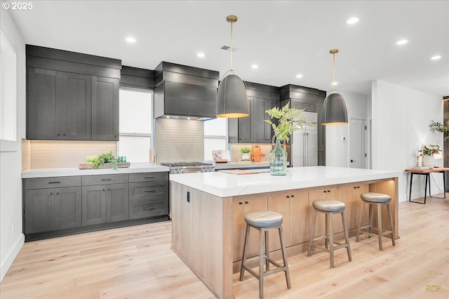 kitchen with light stone countertops, light wood-type flooring, premium range hood, a spacious island, and hanging light fixtures