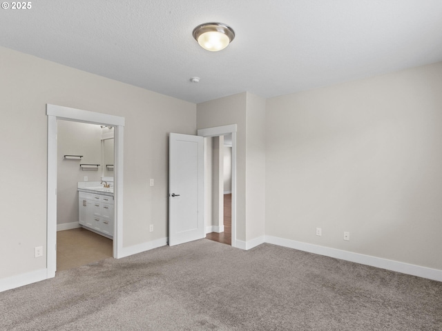 unfurnished bedroom with light carpet, sink, a textured ceiling, and ensuite bathroom