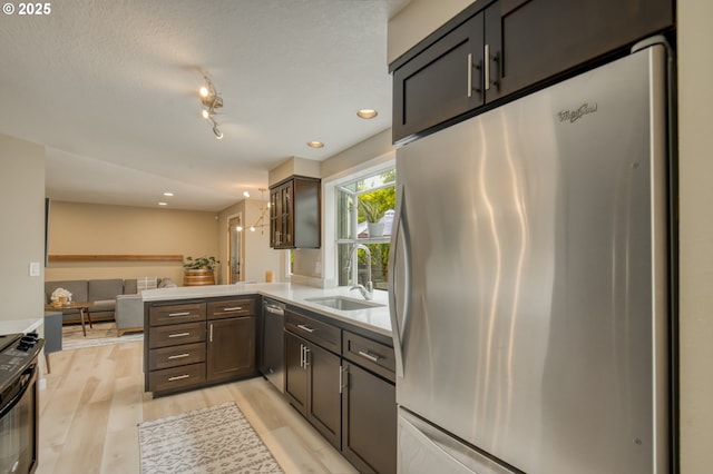 kitchen with stainless steel appliances, a sink, a peninsula, open floor plan, and light countertops
