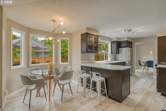 kitchen featuring a chandelier, freestanding refrigerator, light countertops, glass insert cabinets, and baseboards
