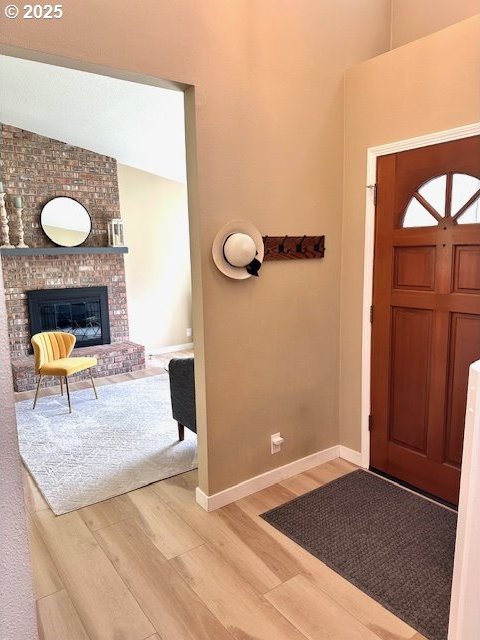 entryway featuring wood finished floors, baseboards, and a brick fireplace