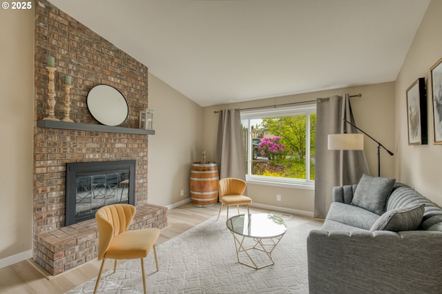living area with wood finished floors, vaulted ceiling, baseboards, and a brick fireplace