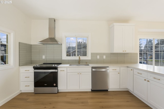 kitchen with wall chimney range hood, sink, appliances with stainless steel finishes, white cabinets, and light wood-type flooring