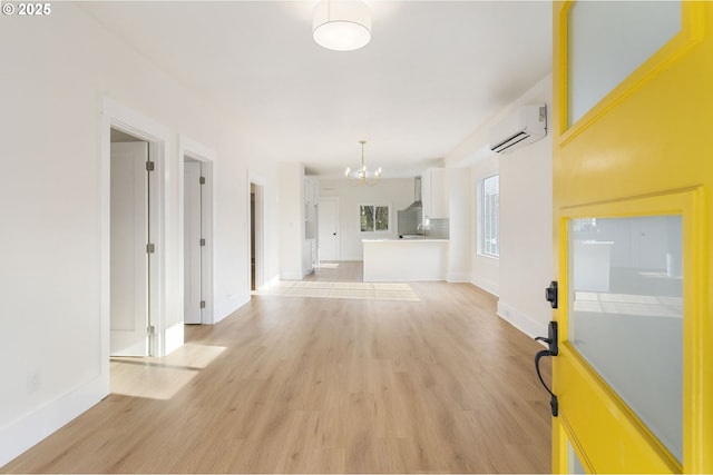 unfurnished living room with an inviting chandelier, light hardwood / wood-style floors, and a wall mounted AC