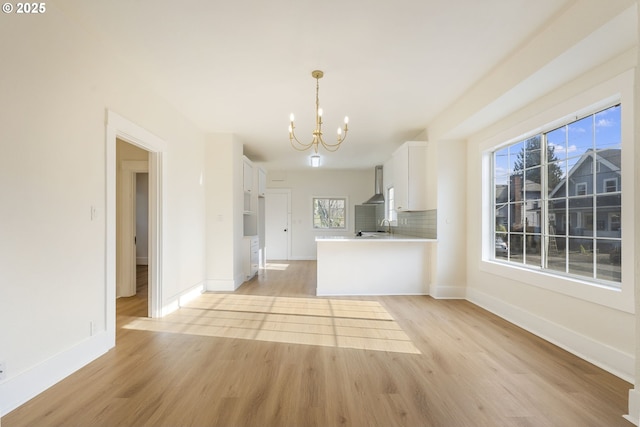 unfurnished living room featuring an inviting chandelier, sink, and light hardwood / wood-style flooring