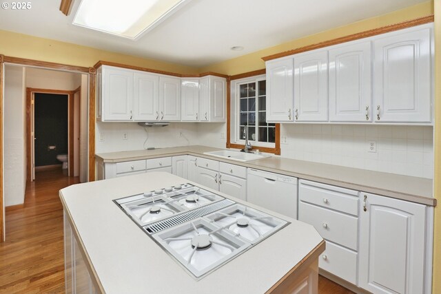 kitchen with a sink, white appliances, a center island, white cabinets, and light wood finished floors